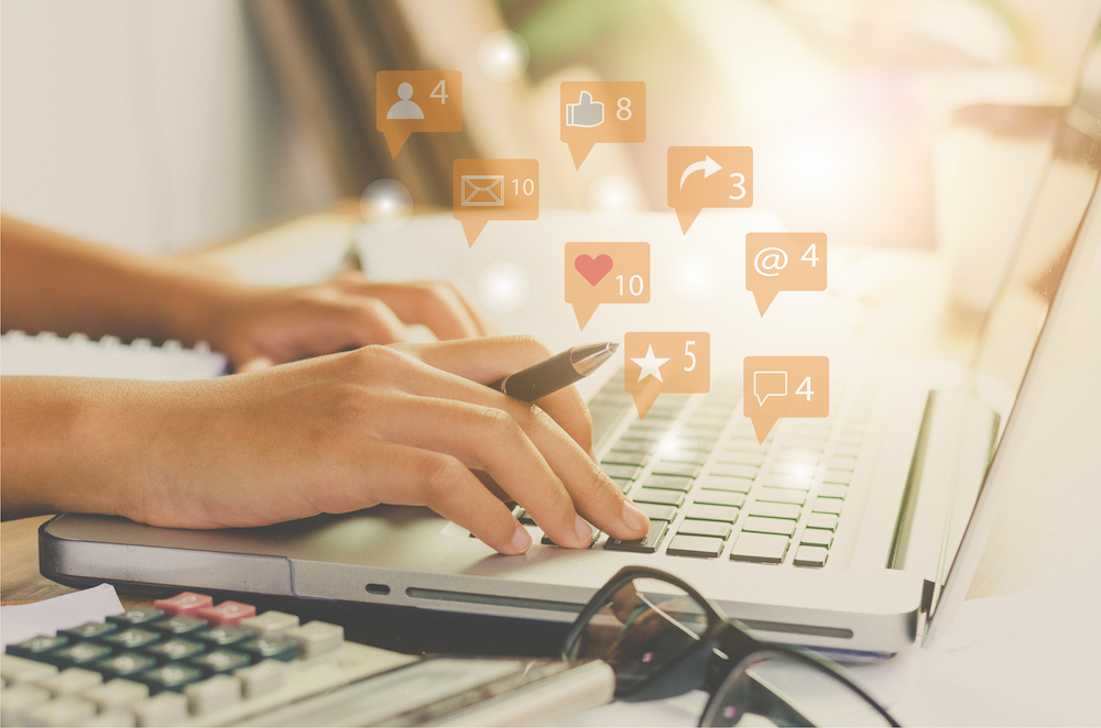 Hands on laptop keyboard with floating comment balloons showing reaction icons