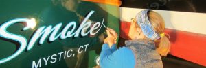 Sarah Brandon hand lettering the name Smoke on the back of a boat