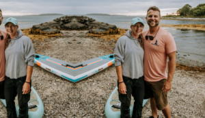 Phillip Browne of Skipper Services, a boat tour small business, stands with a women on a rocky Maine beach.