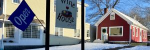 External photo of Wine House on Main's red building and large sign with logo and open flag.