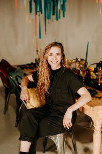 White women smiling in black jumpsuit sits at a table she set for a formal event