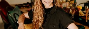 White women smiling in black jumpsuit sits at a table she set for a formal event