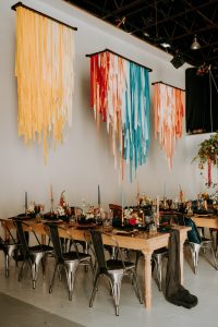 Formal event with table settings and spreads, colorful installations hang in the air above the tables also