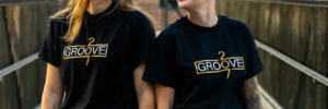 Groove 207 owners, two women smiling at each other wearing shirts with Groove 207 Logo, white and gold type on black background