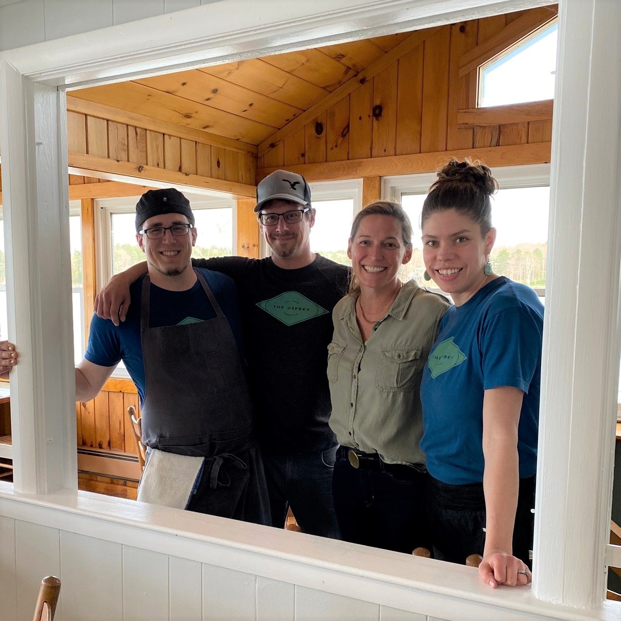 Group Photo of The Osprey Resturant, two white men and two white women with their arms around each other inside a restaurant doorway.