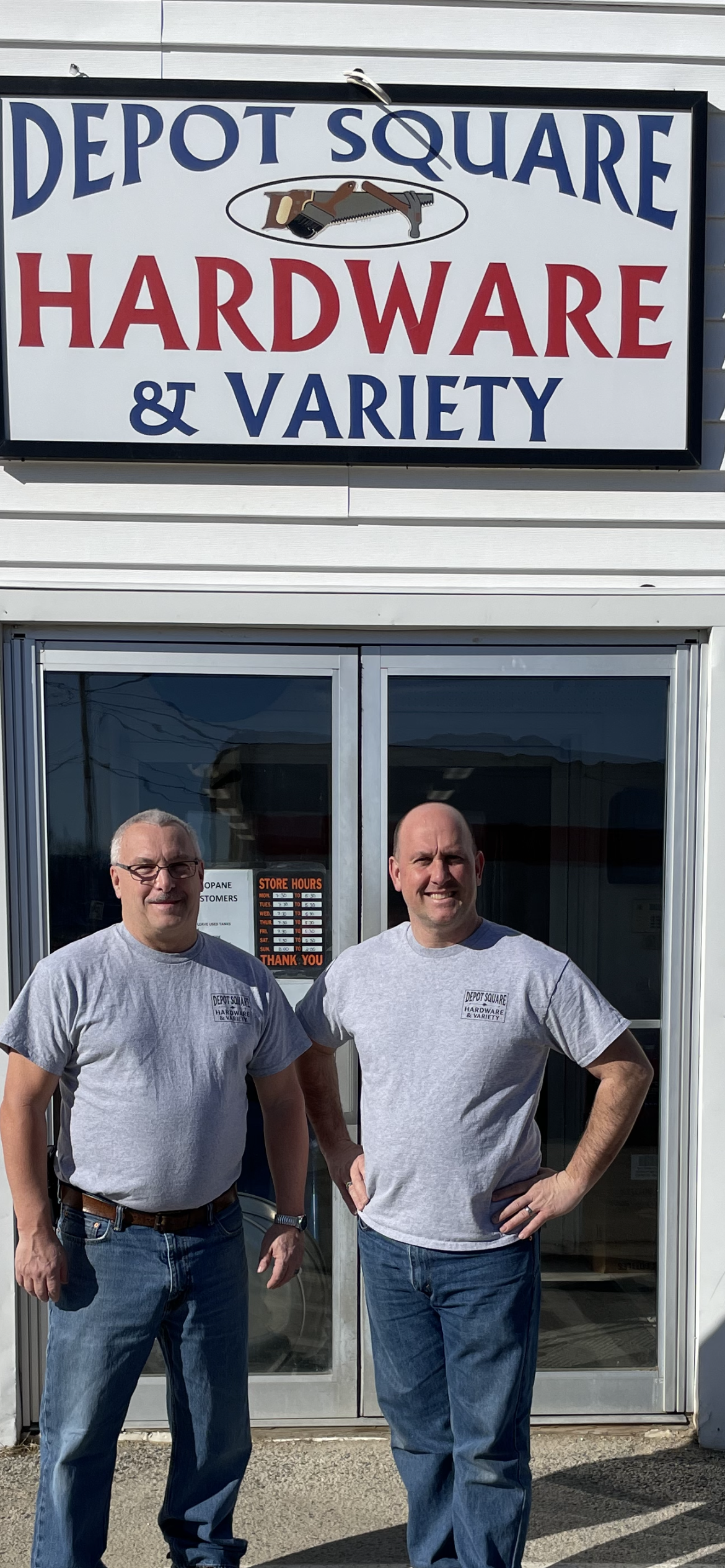 Chad Boulet (right) and Scott Hunter(left) proudly stand in front of their store front, below a sign that reads Depot Square Hardware & Variety. 