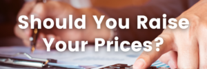 Should You Raise Your Prices? text over an image hands working at a desk writing and using a calculator