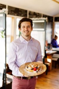 Owner Michael Begley holds a waffle inside of Peace, Love, Waffles, a Dover-Foxcroft Small Business, photo by Sienna Renee Photography