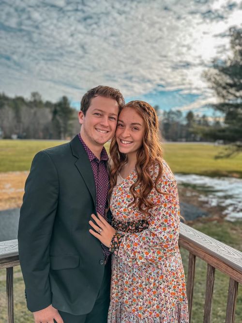 Noah and Ashley Sixberry, a young couple stand close to each other outside in front of a Maine background.