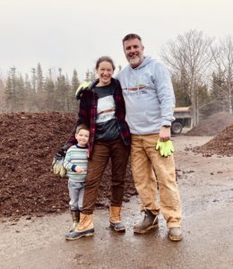 Katie and Matt Saunders stand with their young on in front of compost pile
