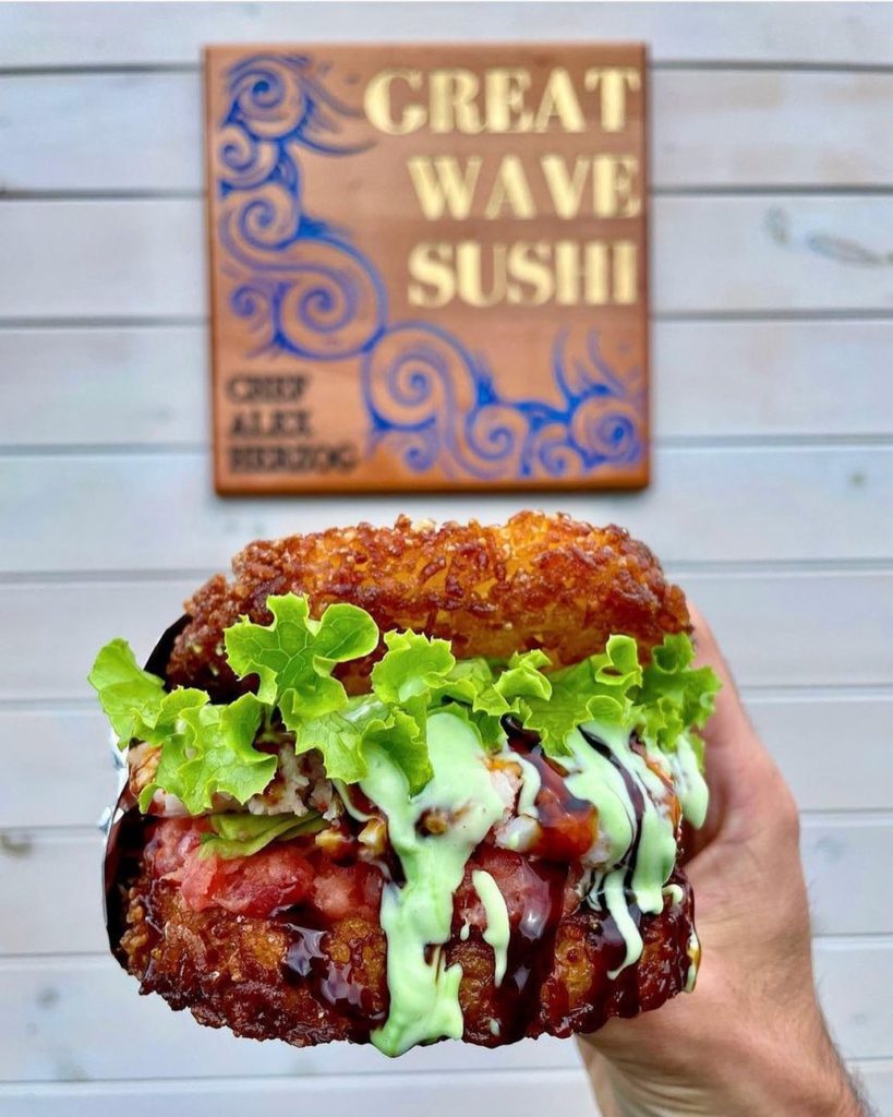 Sushi burger from Great Wave Sushi - hand holding burger in front of the Great Wave Sushi sign