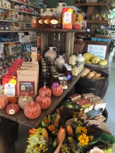 Store display at A&B Naturals which includes various fall seasonal products on wooden stand including fall floral arrangements, candles, coffee, caramels, maple syrup and more.