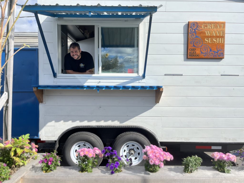 White food truck with man inside smiling, Great Wave Sushi food struck with flowers