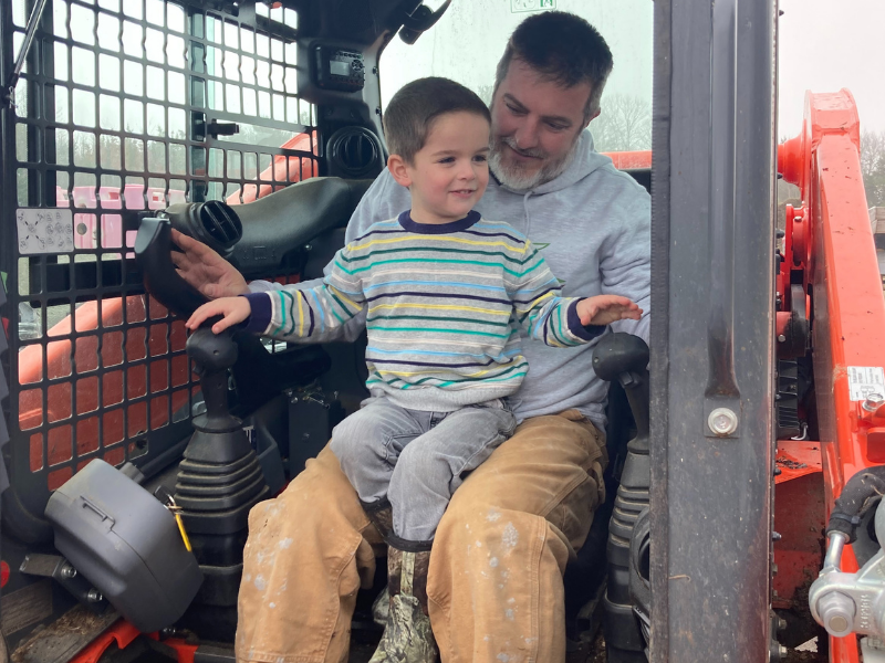 Matt Saunders with young son on machine at their composting business, 1 Earth Composting