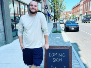 Zachary Brann of Main Street Provisions standing outside his location with a "Coming Soon" sign