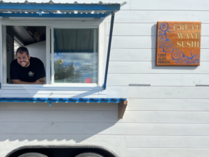 Alex Herzog smiling happily in the window of his newly finished food truck with Great Wave Sushi sign