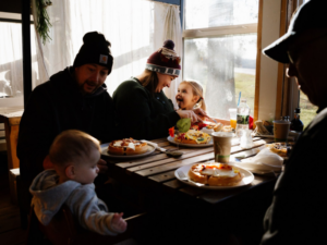 Family with three adults and two young children happily eating a variety of waffles at Peace, Love, Waffles